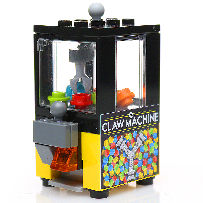 Minifig-Scale Arcade Claw Machine Building Set made from LEGO parts by B3 Customs, featuring a detailed claw machine model with colorful pieces inside and a joystick control.