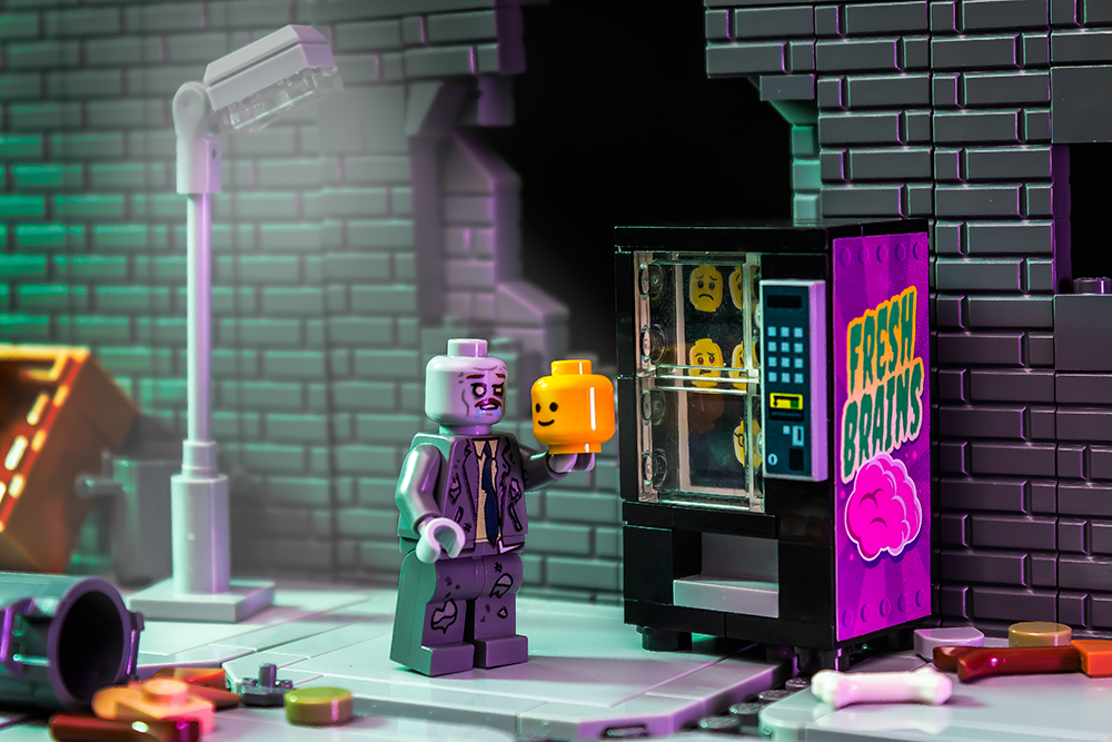 Fresh Brains Zombie Vending Machine w/ Zombie Minifig by B3 Customs featuring a custom LEGO zombie holding a minifigure head next to a detailed vending machine labeled "Fresh Brains" on a brick street scene.
