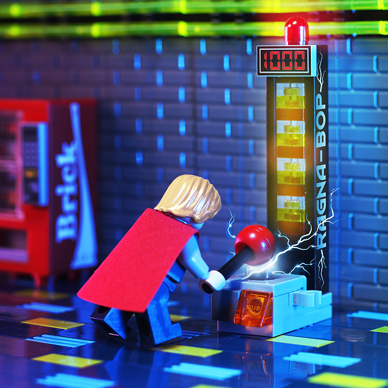 Minifigure playing the Ragna-Bop - B3 Customs Strongman Amusement Park Game with glowing impacts, showcasing custom LEGO bricks by vendor B3 Customs in a vibrant arcade setting.