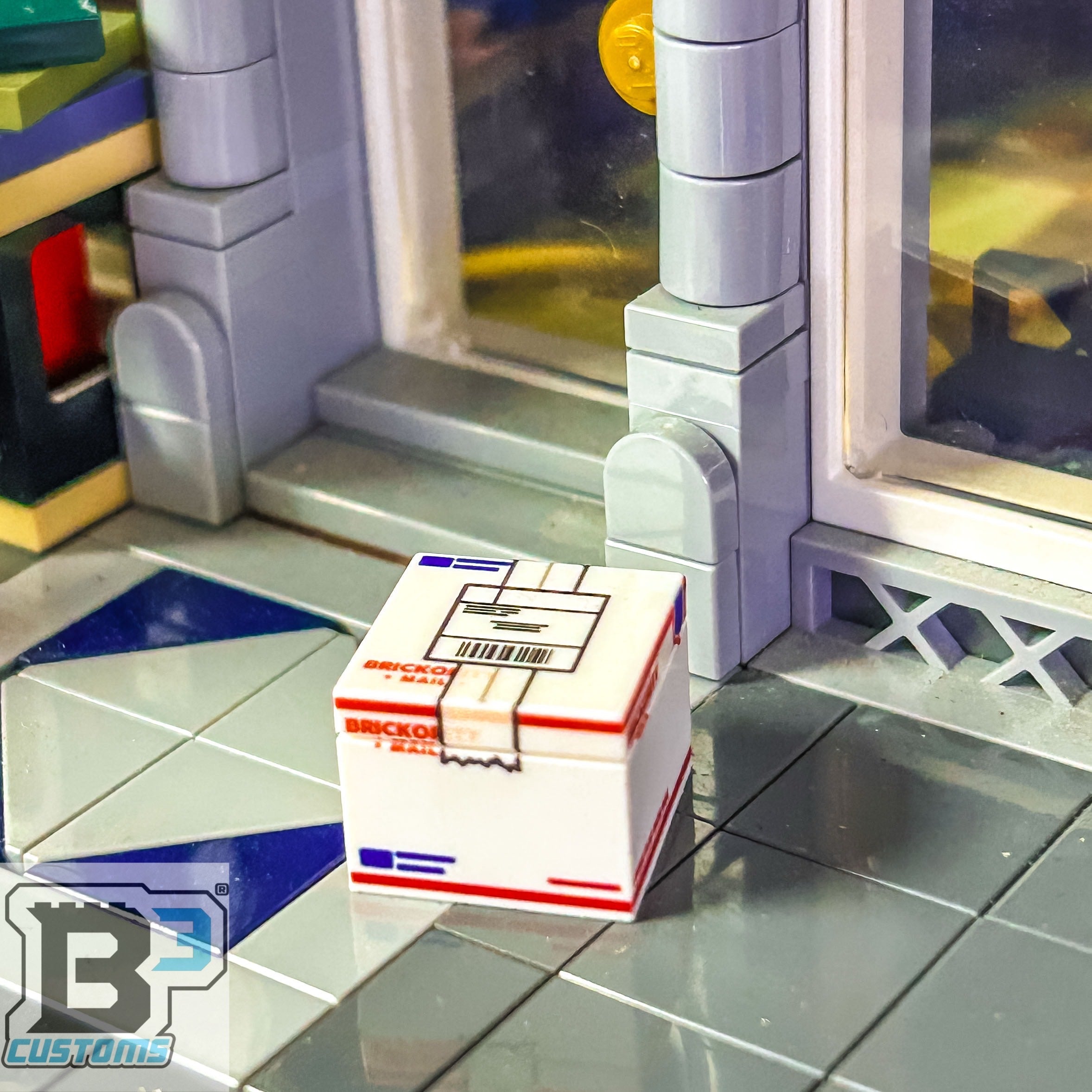 A detailed USPS Priority Shipping Box - Custom Printed made using LEGO parts by B3 Customs, displayed on a tiled floor near a building entrance with glass doors.
