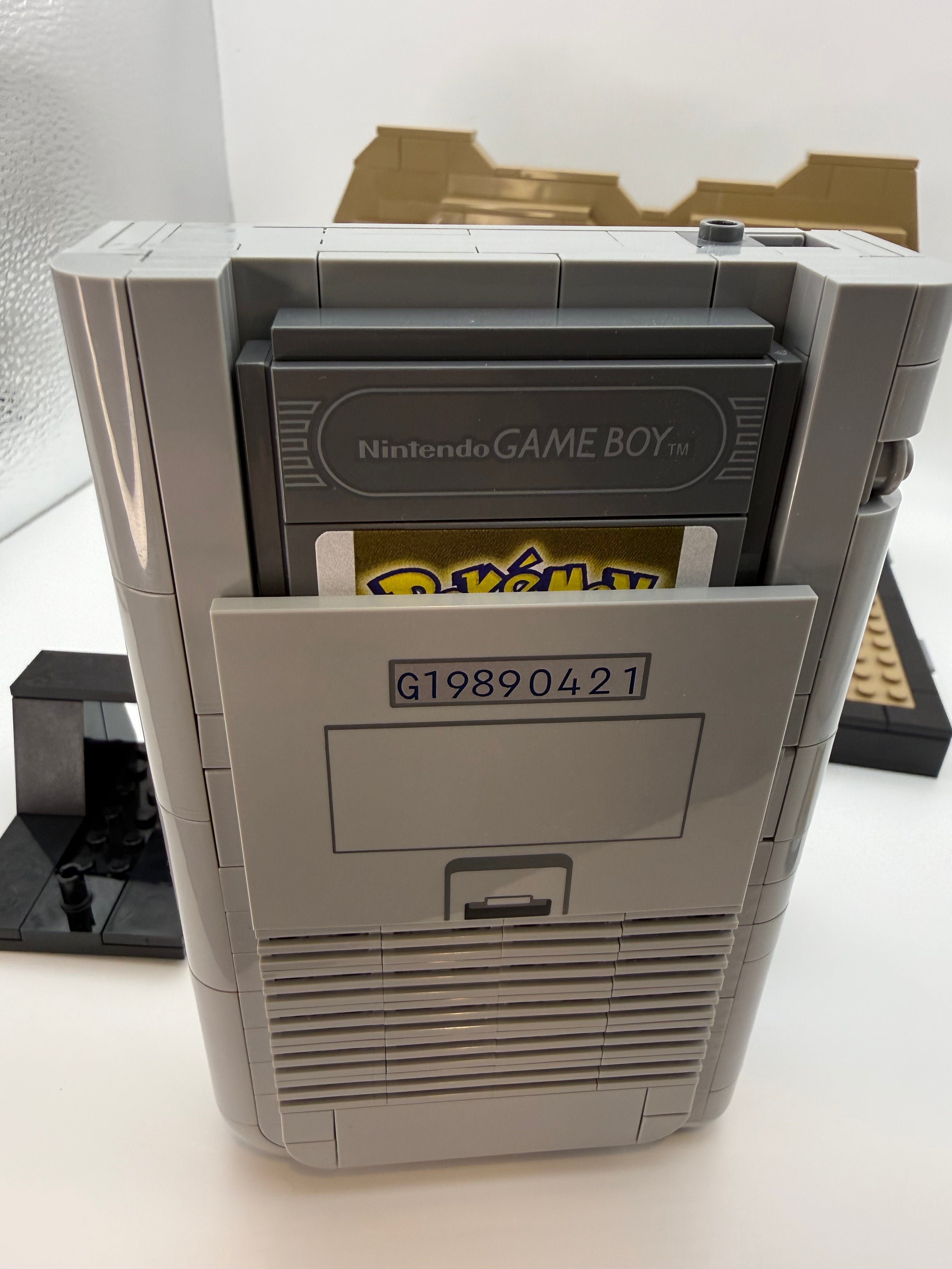 A custom-built retro Nintendo Game Boy model made from LEGO bricks, featuring a detailed cartridge slot with a visible Pokémon game cartridge, enhanced by the Printed Tile Upgrade Kit for GB Set Game Cartridge.
