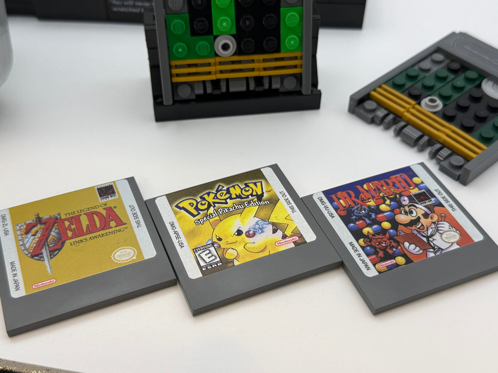 Three classic gray game cartridges featuring printed tile labels, displayed alongside custom LEGO builds, showcasing the Printed Tile Upgrade Kit for GB Set Game Cartridge.