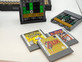 Three custom LEGO game cartridges featuring printed tiles resembling classic games like Pokémon, Mario World, and The Legend of Zelda displayed alongside brick-built game consoles using the Printed Tile Upgrade Kit for GB Set Game Cartridge.