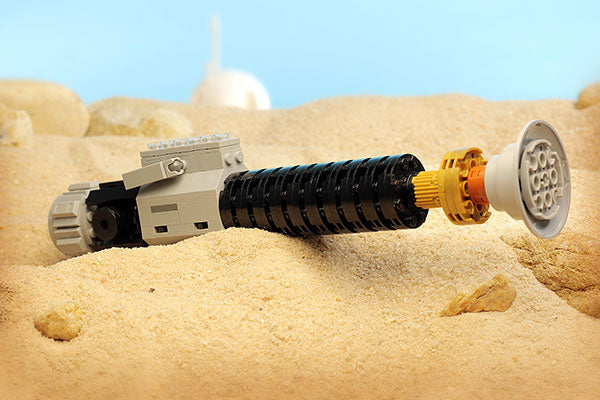 Obi-Wan Lightsaber w/ Stand made with LEGO parts displayed on a sandy surface resembling a desert landscape, showcasing detailed brick construction.