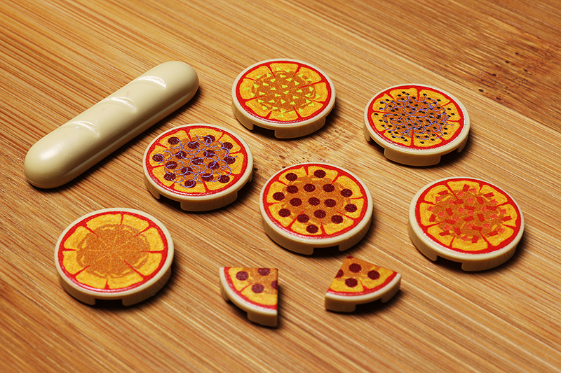 Various colorful LEGO tile pieces designed to resemble different pizza styles and slices, part of the Pizza Pack made using LEGO parts - B3 Customs displayed on a wooden surface.