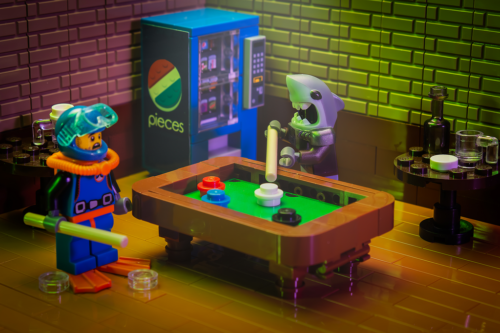 A detailed scene featuring the Pool Table Building Kit made from LEGO parts by B3 Customs, showing two LEGO minifigures playing pool in a colorful arcade setting with a vending machine and bar tables in the background.