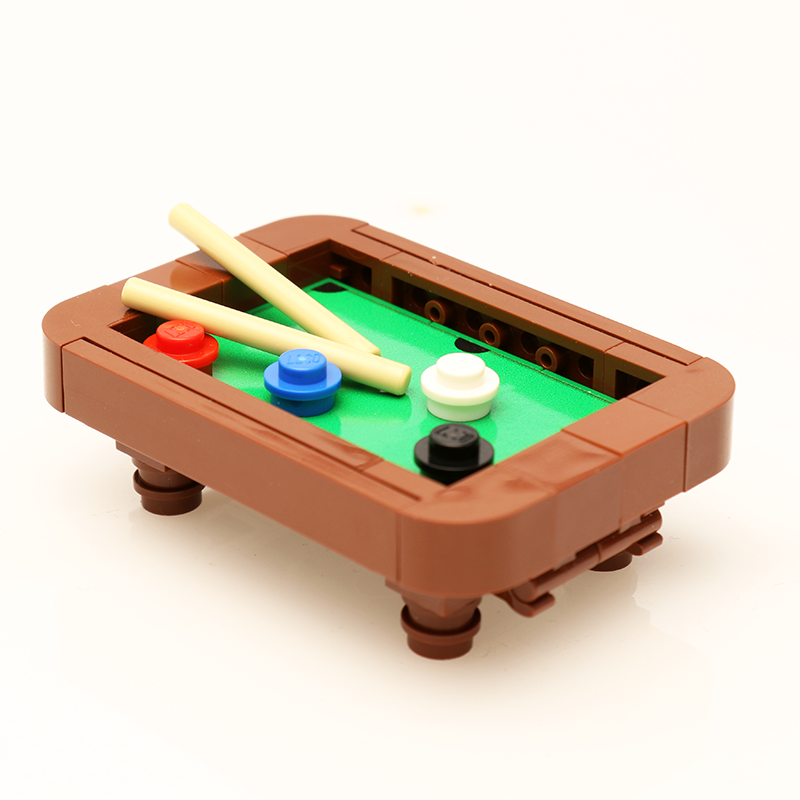 Close-up of a small pool table built from brown and green LEGO bricks with two beige cues and colored round pieces, part of the Pool Table Building Kit made from LEGO parts by B3 Customs.