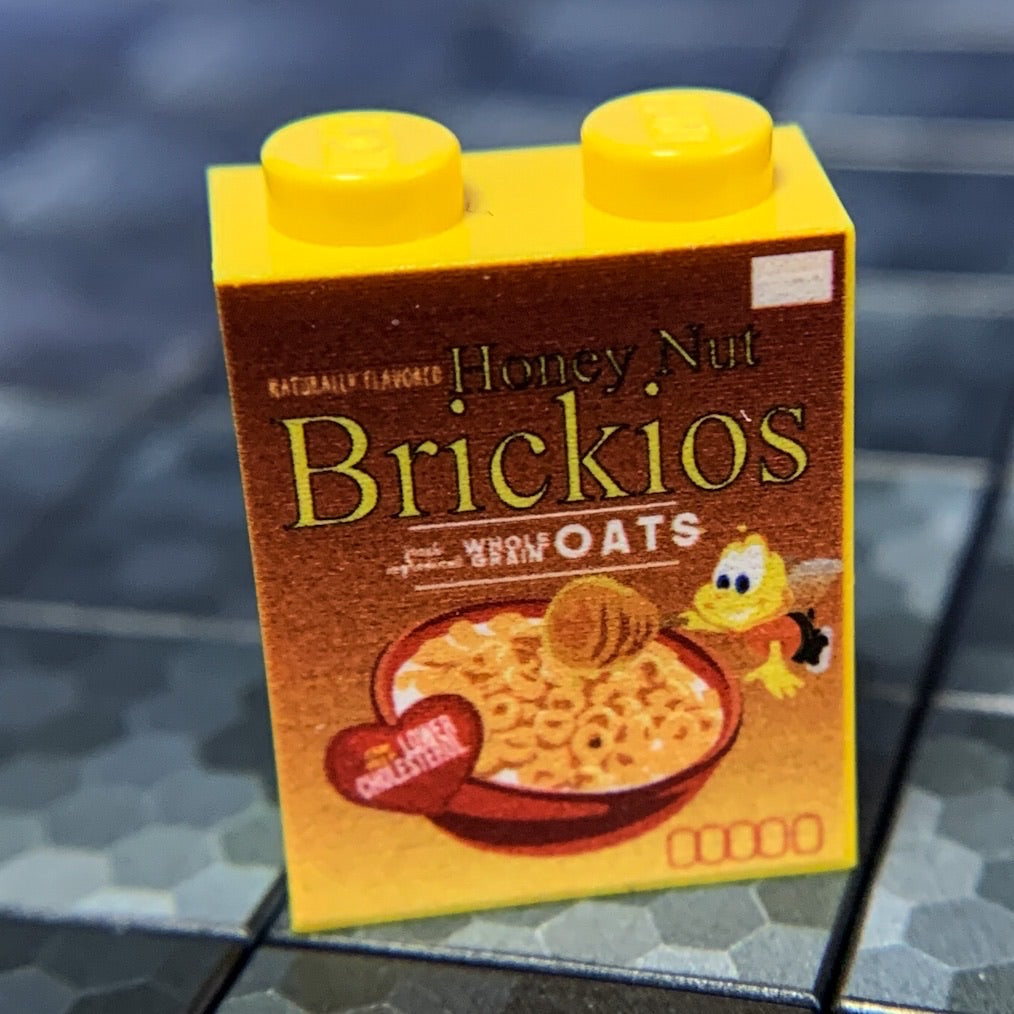 Yellow custom printed LEGO brick resembling a Honey Nut Brickios Cereal box with detailed graphics, part of the Honey Nut Brickios Cereal Custom Printed 1x2x2 Brick made using LEGO part - B3 Customs collection.